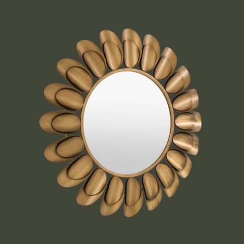 Round decorative wall mirror with a sculpted gold petal-inspired frame in a modern sunburst design against a dark neutral background.