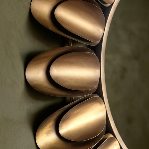 Close-up detail of a decorative round mirror with layered gold-toned petal accents and brushed metallic finish.