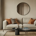 Modern living room with a beige sofa, round black mirror, and decorative items.