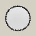 Round wall mirror with a sculptural black beaded frame and contemporary design against a soft neutral background.