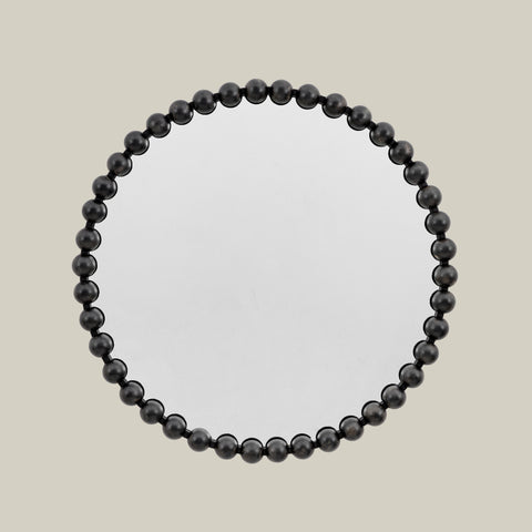 Round wall mirror with a sculptural black beaded frame and contemporary design against a soft neutral background.