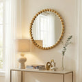 Decorative rounded wall mirror with a sculptural gold beaded frame displayed above a console table in a bright contemporary interior.