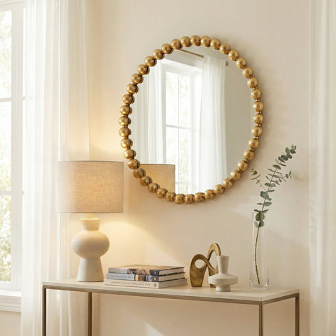 Modern statement mirror with rounded silhouette and gold beaded frame in a soft neutral living space.