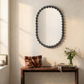 Modern statement mirror with rounded silhouette and black beaded frame above a console table with floral decor.