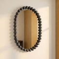 Modern statement mirror with rounded silhouette and black beaded frame against a softly lit neutral wall.