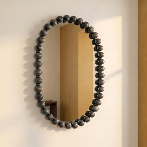 Modern statement mirror with rounded silhouette and black beaded frame against a softly lit neutral wall.