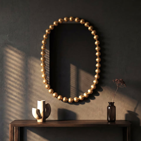 Luxury wall mirror featuring a sculptural gold ball frame with warm natural light and minimalist decor.