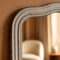 Close-up detail of a distressed grey mirror frame featuring a softly curved silhouette, delicate beaded trim and vintage-inspired texture.