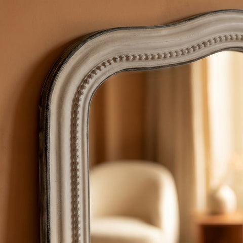 Close-up detail of a distressed grey mirror frame featuring a softly curved silhouette, delicate beaded trim and vintage-inspired texture.