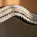 Macro shot of a shaped grey mirror frame highlighting subtle distressing and refined beaded accents.