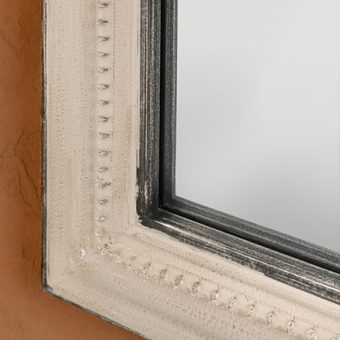 Decorative mirror frame detail with a softly distressed grey finish, delicate beading and contrasting aged trim.