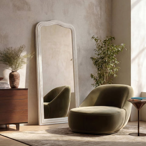 Leaner-style white floor mirror with a softly curved silhouette, distressed finish and delicate beaded detailing, styled in a warm, neutral interior