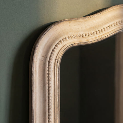 Close-up detail of a distressed mirror frame featuring a softly curved silhouette, decorative beaded trim and vintage-inspired texture.