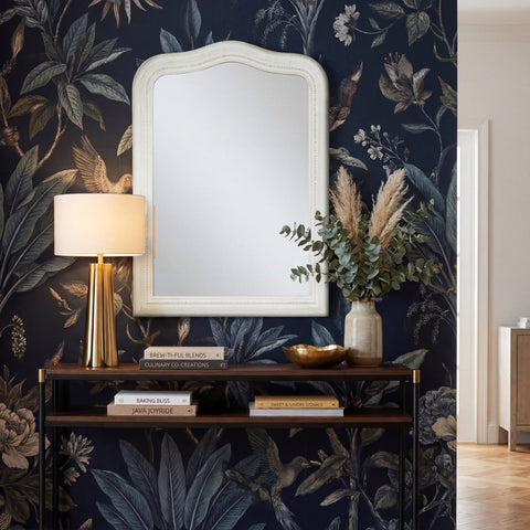 Decorative white wall mirror, distressed finish, styled against dark botanical wallpaper above a console table.