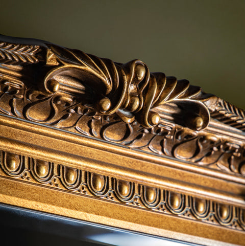 Detailed view of a vintage-style gold mirror frame featuring elaborate baroque-inspired carvings.