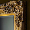Close-up detail of an ornate antique gold mirror frame with intricate carved scrollwork and decorative embossed patterns.