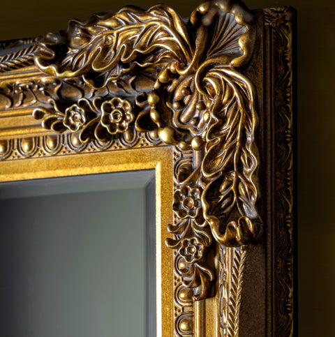 Close-up detail of an ornate antique gold mirror frame with intricate carved scrollwork and decorative embossed patterns.