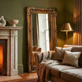Vintage-style standing mirror with an intricate gold frame in a cosy luxury interior with fireplace and soft lighting.