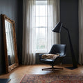 Large ornate gold full-length floor mirror leaning beside a modern black lounge chair and floor lamp in a sophisticated dark interior.