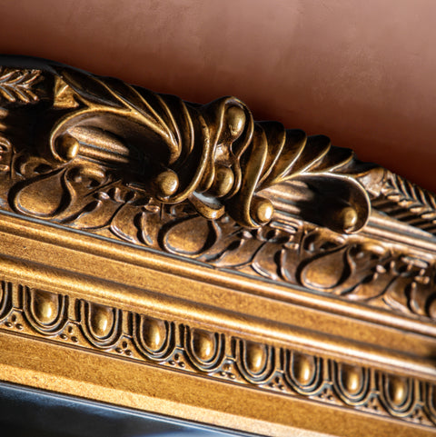 Close-up of decorative gold mirror trim with intricate ornamental detailing and textured metallic finish.