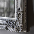 Detailed view of a vintage-style silver mirror frame with embossed ornamental carvings.