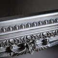 Close-up detail of an ornate antique silver mirror frame with intricate carved patterns and decorative metallic finish.