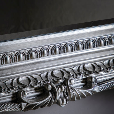 Close-up detail of an ornate antique silver mirror frame with intricate carved patterns and decorative metallic finish.