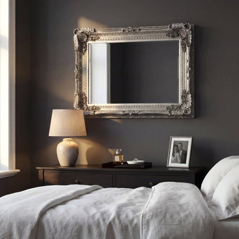 Vintage-style silver wall mirror with intricate baroque detailing in a sophisticated bedroom interior.