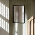 Black-framed mirror on a wall with sunlight casting shadows