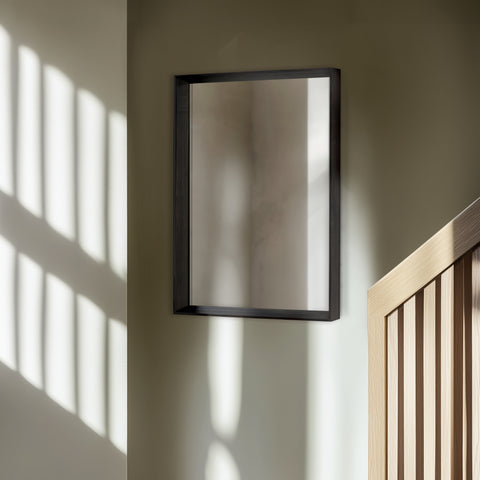 Black-framed mirror on a wall with sunlight casting shadows