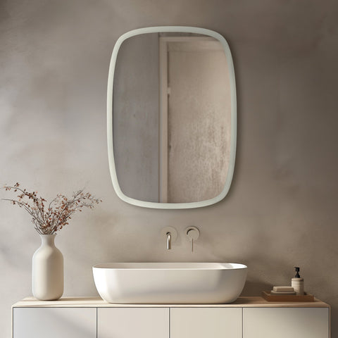 Irregular rounded rectangular wall mirror with a slim white frame displayed above a modern vessel sink in a minimalist neutral bathroom.