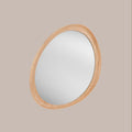 Round organic shaped mirror with a oak wooden frame forward facing on a beige background