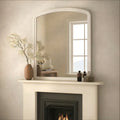 White framed over-mantel mirror above a fireplace with decorative items on a mantel.