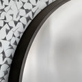 Close-up of a round mirror with a black frame and a patterned white and black design wallpaper behind.