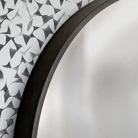 Close-up of a round mirror with a black frame and a patterned white and black design wallpaper behind.