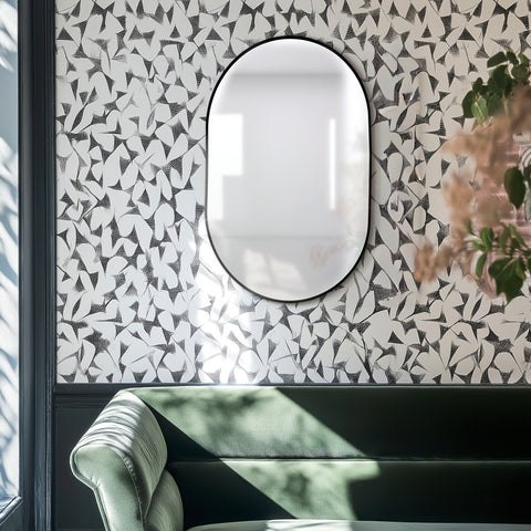 Pill shaped decorative black framed mirror on a wall above a green sofa