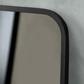 Close-up detail of a dark-framed mirror featuring softly rounded corners, subtle texture and clean contemporary styling.
