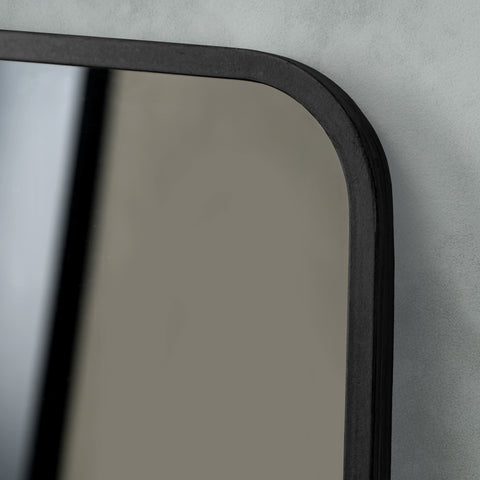 Close-up detail of a dark-framed mirror featuring softly rounded corners, subtle texture and clean contemporary styling.