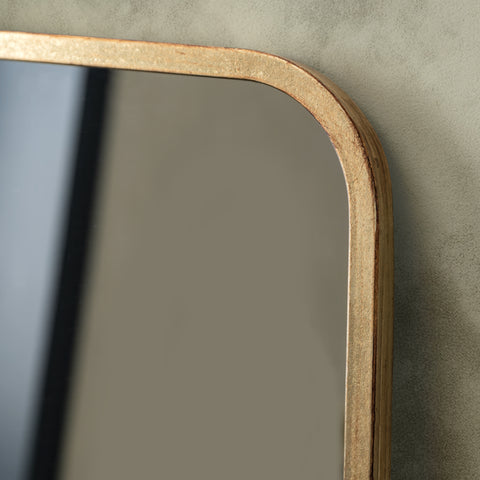 close up of a rectangular leaner mirror with a gold effect frame on a green wall