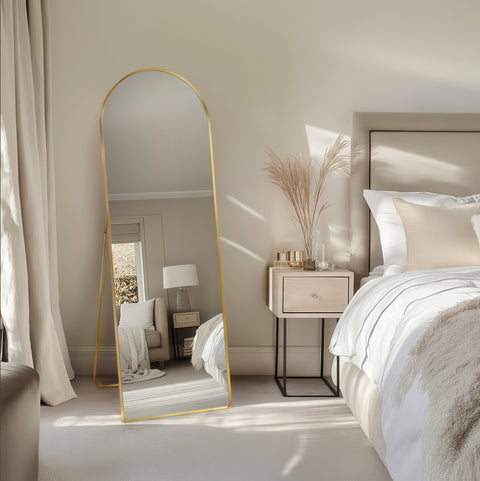 Neatly arranged bedroom with a free standing gold mirror, bed, and side table.