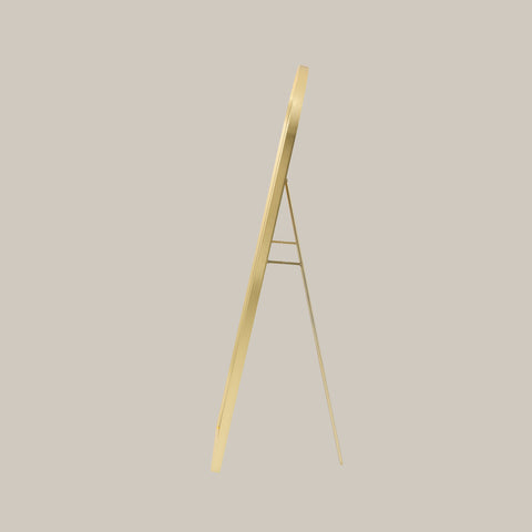 cheval arched mirror with gold frame shown from the side angle on a beige background