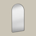 Arched leaner mirror with black frame on a beige wall set at an angle