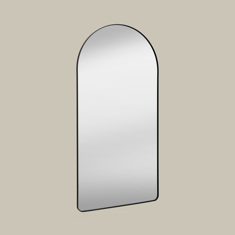 Arched leaner mirror with black frame on a beige wall set at an angle