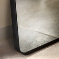 Close-up of a rectangular rounded edge leaner mirror with a black frame on a light-coloured floor.