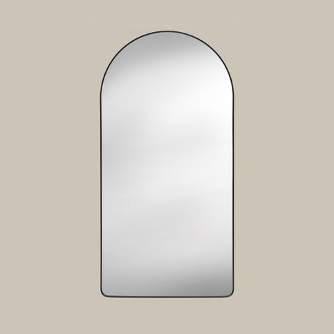 Arched leaner mirror with black frame on a beige wall