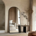 Modern interior with a tall floor leaner mirror with a black frame, a small table with decorative items, and a chair.