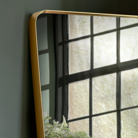 Detailed corner view of a gold metal mirror frame showcasing smooth curves and a refined brushed finish.
