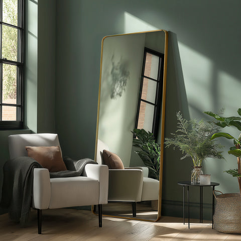 Contemporary gold leaner mirror with a slim frame, styled beside soft furnishings and natural greenery for a calm modern look.