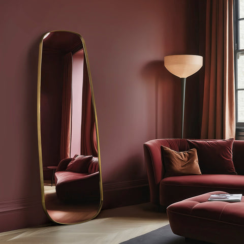 Living room with a tall mirror, red sofa, and lamp against a dark pink wall.