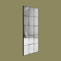 Tall rectangular antiqued panel wall mirror with black metal grid detailing and distressed vintage-style glass against a muted olive background.